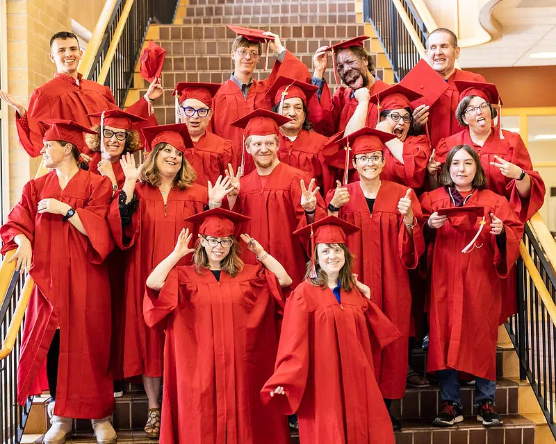 ALU Graduates pose for a silly photo on a staircase in red cap and gown.